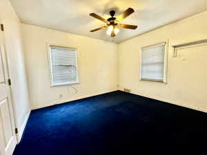 Spare room featuring dark colored carpet, ceiling fan, and a textured ceiling