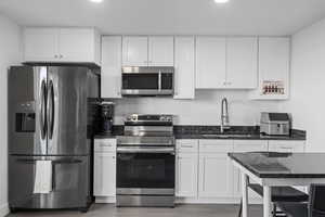 Kitchen featuring a kitchen breakfast bar, stainless steel appliances, dark wood-type flooring, sink, and white cabinetry