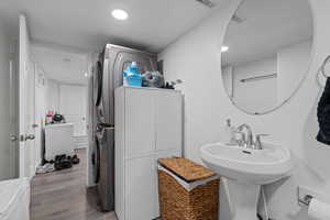 Bathroom with stacked washer / drying machine, wood-type flooring, and sink