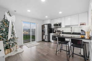 Kitchen with dark stone counters, sink, hardwood / wood-style flooring, white cabinetry, and stainless steel appliances