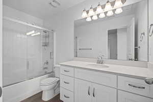 Full bathroom featuring shower / bath combination with glass door, toilet, vanity, and hardwood / wood-style flooring