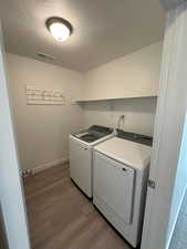 Laundry area featuring hardwood / wood-style flooring, independent washer and dryer, and a textured ceiling