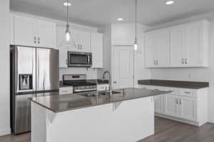 Kitchen featuring decorative light fixtures, stainless steel appliances, a kitchen island with sink, and sink