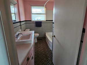 Bathroom with a washtub, vanity, tile walls, and toilet