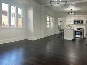 Kitchen with stainless steel appliances, white cabinetry, dark hardwood / wood-style floors, and a healthy amount of sunlight