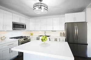 Kitchen featuring stainless steel appliances, white cabinetry, hanging light fixtures, and sink