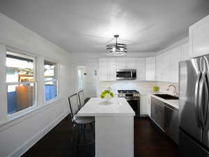 Kitchen featuring appliances with stainless steel finishes, white cabinetry, a kitchen island, and hanging light fixtures