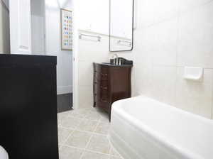 Bathroom with tile patterned floors, a tub to relax in, vanity, and tile walls