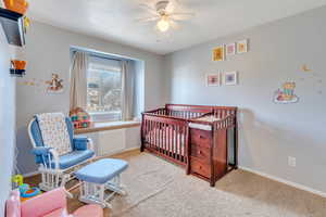 Bedroom with ceiling fan, a nursery area, and light carpet