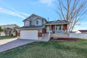 Split level home featuring covered porch, a garage, and a front lawn