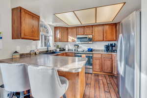 Kitchen with sink, a kitchen breakfast bar, dark hardwood / wood-style flooring, kitchen peninsula, and appliances with stainless steel finishes