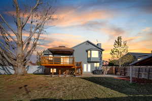 Back house at dusk with french doors, a wooden deck, a gazebo, a patio, and a lawn