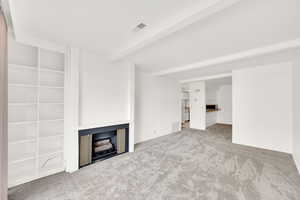 Unfurnished living room featuring beamed ceiling and carpet floors