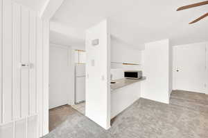 Kitchen with ceiling fan, white cabinets, light colored carpet, and white refrigerator