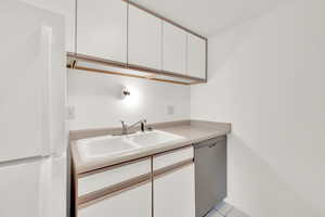 Kitchen with white cabinetry, dishwasher, sink, white refrigerator, and light tile patterned floors