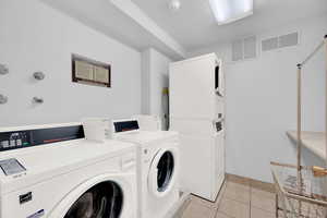 Laundry area with washing machine and dryer, stacked washer and clothes dryer, and light tile patterned flooring