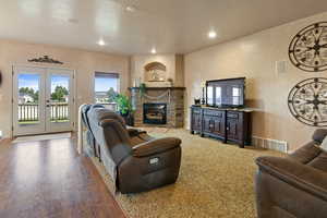 Living room with a stone fireplace, wood-type flooring, a textured ceiling, and french doors