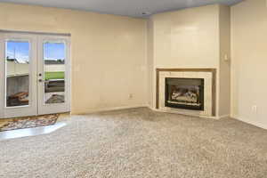 Unfurnished living room with carpet flooring, a tile fireplace, and french doors