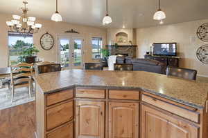 Kitchen with french doors, a stone fireplace, dark hardwood / wood-style floors, a notable chandelier, and pendant lighting