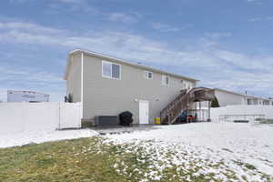 Snow covered rear of property with a yard, central AC, and a wooden deck