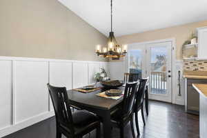 Dining area with dark wood-type flooring, lofted ceiling, and an inviting chandelier