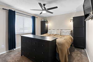 Bedroom featuring ceiling fan, dark carpet, and a textured ceiling