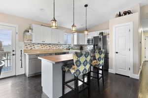 Kitchen featuring dark wood-type flooring, a kitchen island, a kitchen breakfast bar, white cabinets, and appliances with stainless steel finishes