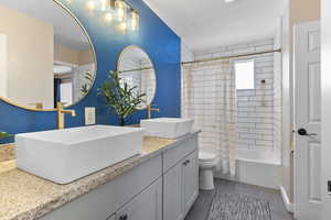 Full bathroom with a textured ceiling, vanity, shower / bath combo with shower curtain, tile patterned flooring, and toilet