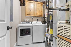 Washroom with washing machine and clothes dryer, water heater, and cabinets