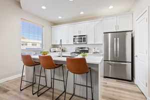 Kitchen with white cabinetry, stainless steel appliances, light hardwood / wood-style floors, a breakfast bar area, and a center island with sink