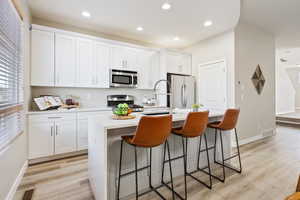 Kitchen with a kitchen island with sink, light wood-type flooring, appliances with stainless steel finishes, a kitchen bar, and white cabinetry