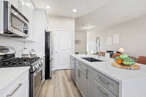 Kitchen with gray cabinetry, stainless steel appliances, sink, white cabinets, and light hardwood / wood-style floors