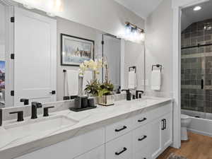 Full bathroom with vanity, vaulted ceiling, shower / bath combination with glass door, hardwood  flooring, and toilet