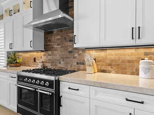 Kitchen featuring wall chimney exhaust hood, white cabinetry, high-end Ilve duel fuel double oven with warming tray.