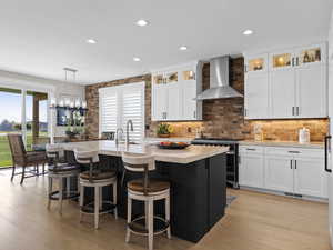 Kitchen featuring a kitchen island with sink, stainless steel gas range, tons of sunlight, and wall chimney range hood