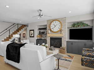 Living room featuring a large fireplace, ceiling fan, light hardwood flooring, and built in cabinets.