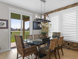 Dining area with a chandelier, light hardwood floors,, brick wall, and plenty of natural light