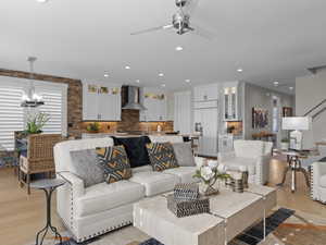 Living room with ceiling fan with notable chandelier and light hardwood floors.