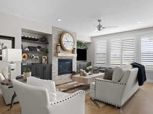 Living room with light wood flooring, a large stacked stone fireplace, and ceiling fan