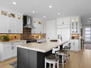 Kitchen with white cabinets, sink, wall chimney exhaust hood, an island with sink, paneled refrigerator, and light hardwood floors.