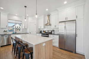 Kitchen featuring hanging light fixtures, light wood-type flooring, wall chimney range hood, and appliances with stainless steel finishes