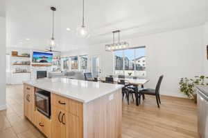 Kitchen with stainless steel microwave, a center island, light brown cabinets, light hardwood / wood-style flooring, and pendant lighting