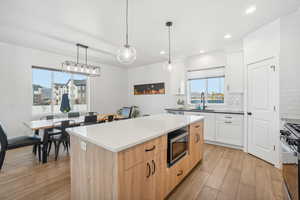 Kitchen featuring stainless steel appliances, sink, pendant lighting, light hardwood / wood-style flooring, and white cabinetry