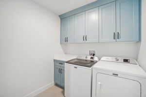 Washroom with washer and clothes dryer, light tile patterned floors, and cabinets