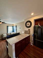 Black fridge with ice dispenser, and kitchen peninsula with seating available from family room side.