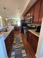This ideal kitchen features wood-flooring, pendant light fixtures, nice, gas appliances with stainless steel and black finishes, and tasteful finishes! Bar seating here.