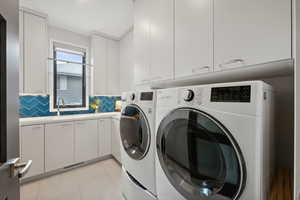 Washroom featuring cabinets, light tile patterned floors, washing machine and dryer, and sink