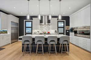 Kitchen with decorative light fixtures, light wood-type flooring, wall chimney range hood, and stainless steel appliances