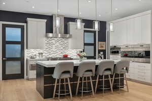 Kitchen with decorative light fixtures, wall chimney range hood, and a large island with sink