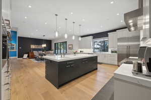 Kitchen with white cabinets, a large island with sink, hanging light fixtures, and stainless steel built in refrigerator